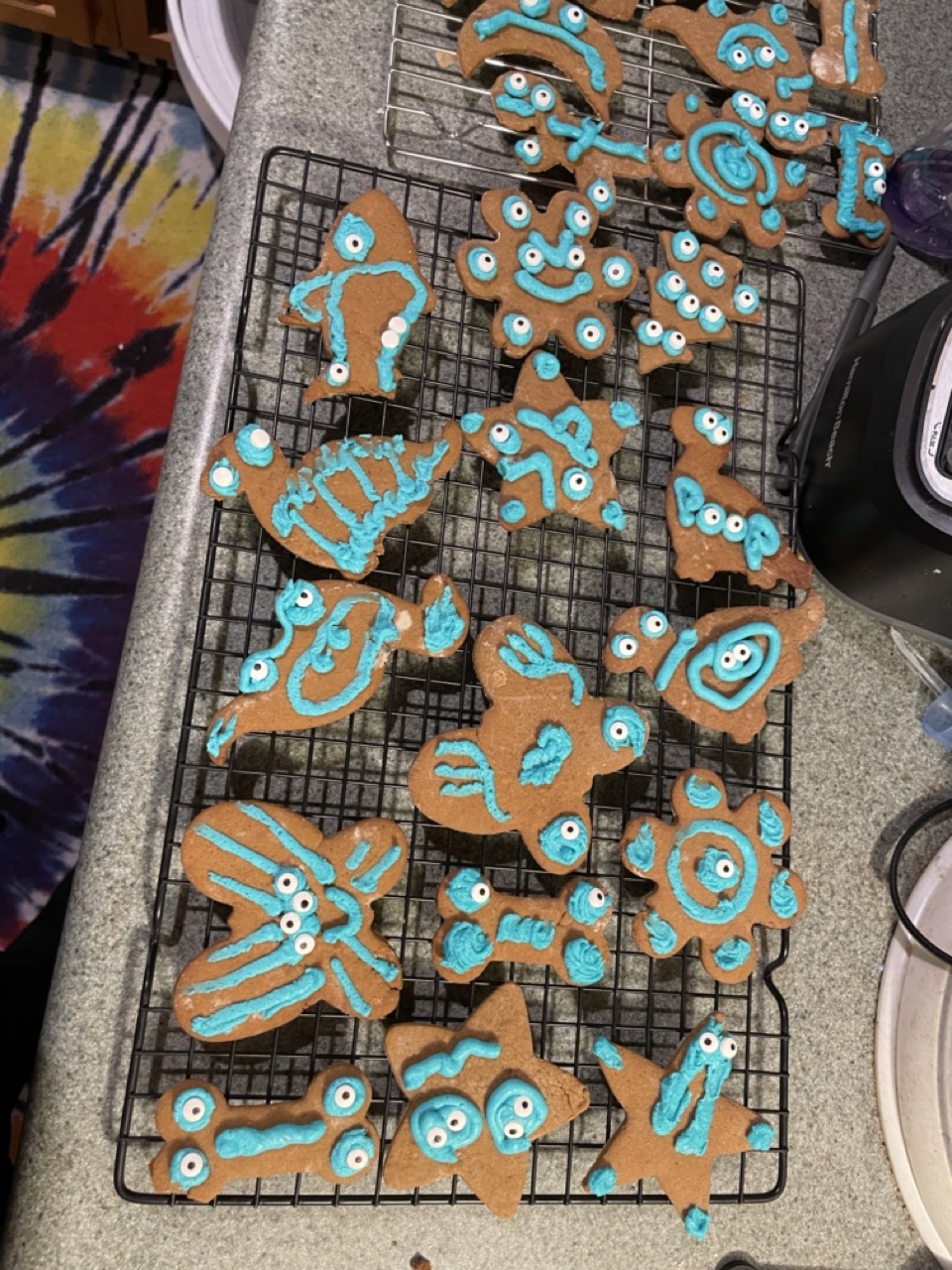 More gingerbread monster cookies with teal icing cooling on a wire rack.